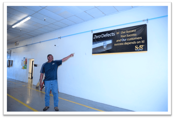 S-5!® manufacturing plant photo of staffer pointing to signage of the zero defects motto