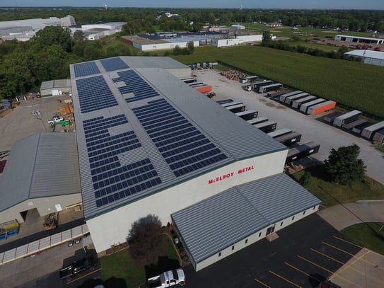 Aerial view of a large metal manufacturing facility with standing seam metal roofs covered in rooftop solar panels, illustrating how solar systems are installed on metal roofs where thermal expansion must be carefully considered.