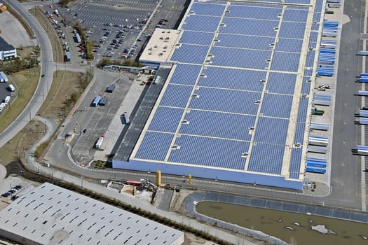 Aerial view of a commercial building with solar panels on a white single-ply membrane roof, promoting energy efficiency.